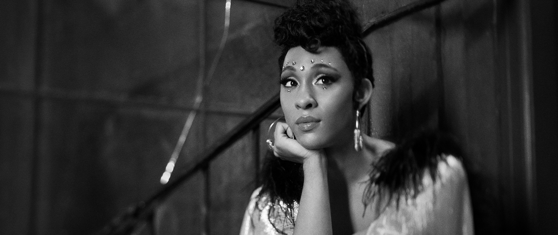 MJ Rodriguez as Blanca in FX's POSE wearing a coat with feathers sitting in a stairway.